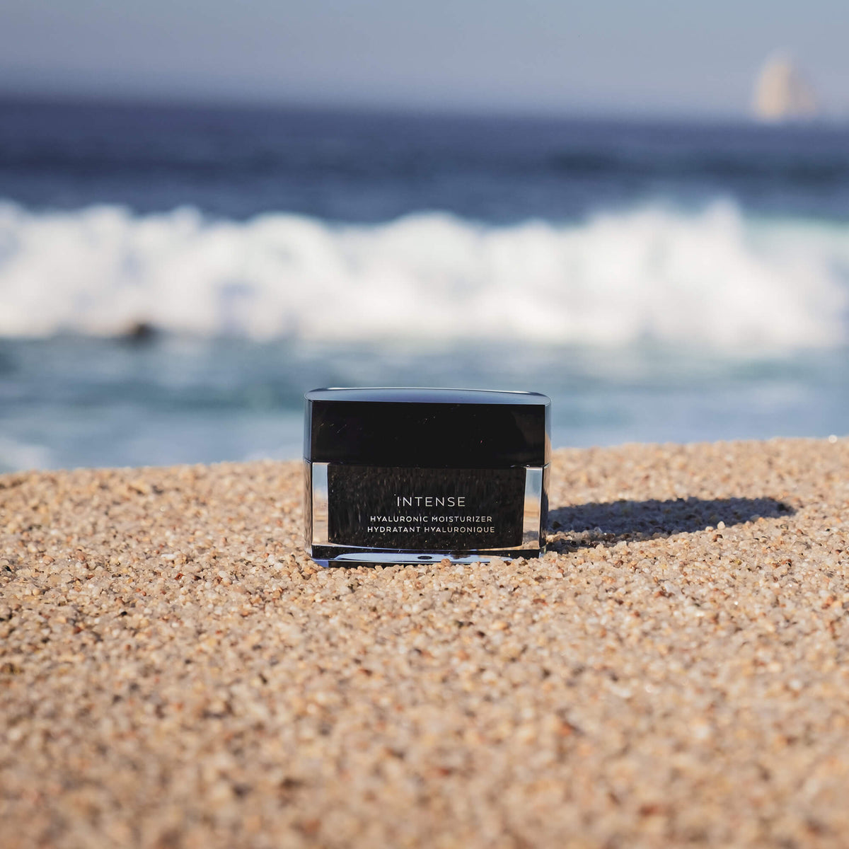 The Barrier Balm jar sitting on sandy beach with ocean waves in the background